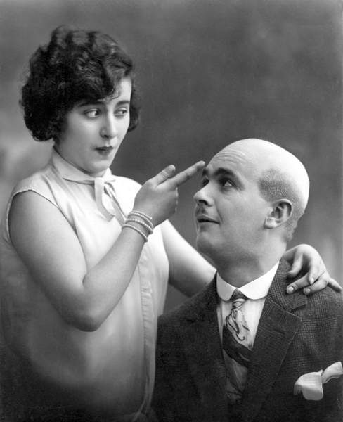 Woman showing with one finger the skull of a bald man: “Why does Egon have no hair? “” . Photography around 1920 / Photo © Imagebroker / Bridgeman Images